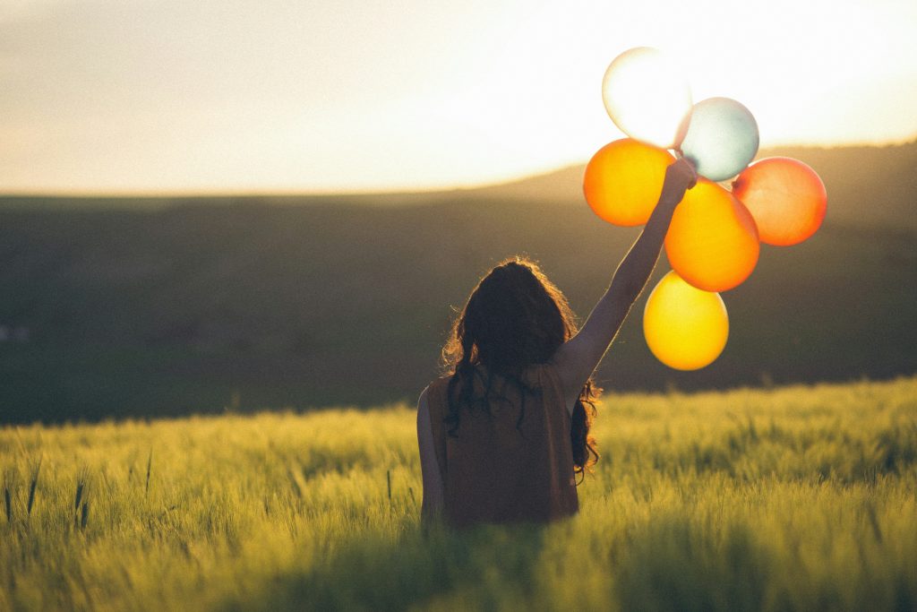kobieta odwrócona tyłem z balonami na łące